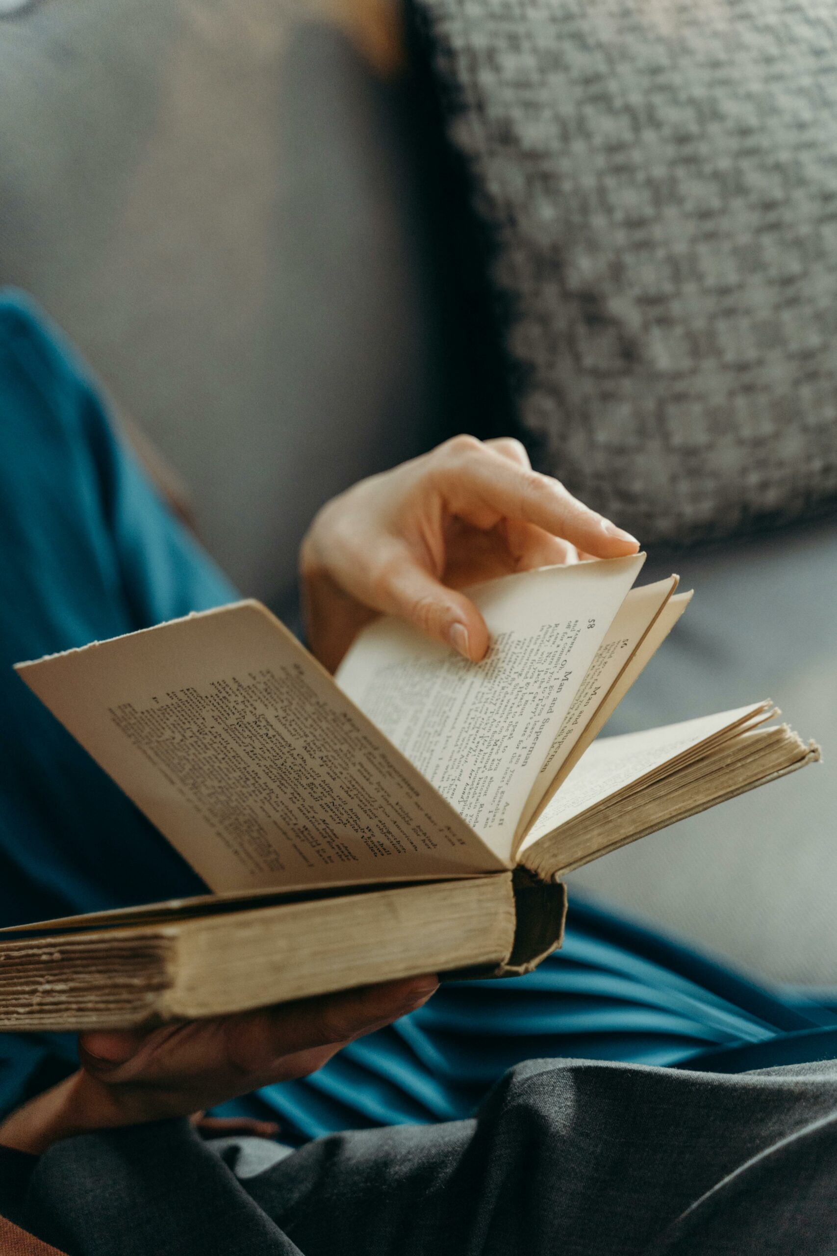A woman in a casual dress reads a book while lounging on a cozy sofa, creating a serene and relaxed atmosphere.